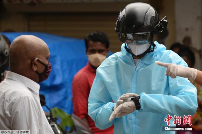 当地时间2020年7月21日，印度孟买，一名非政府组织的卫生工作志愿者穿着防护衣，戴着装有热扫描传感器的智能头盔在居民区挨户查看居民体温。